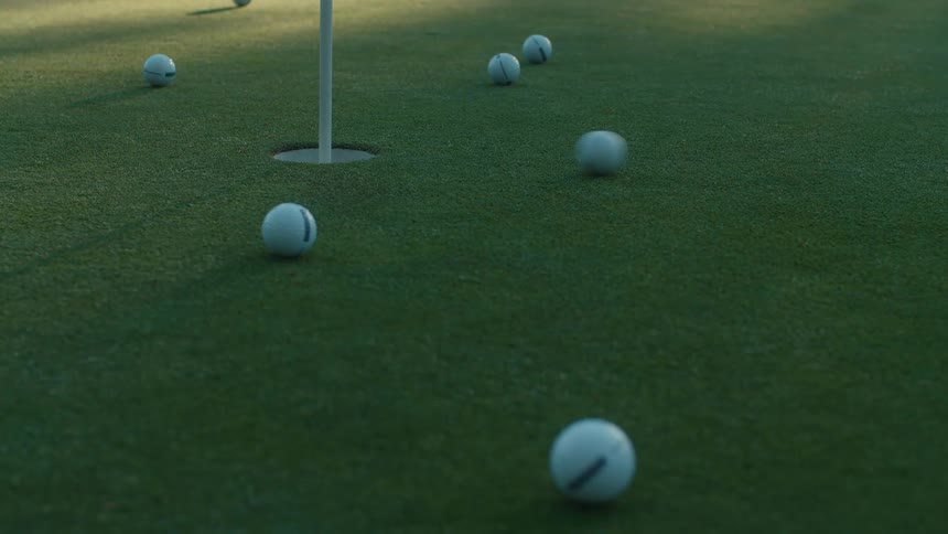 Close up of golf balls rolling across a putting green and missing the hole during a practice session