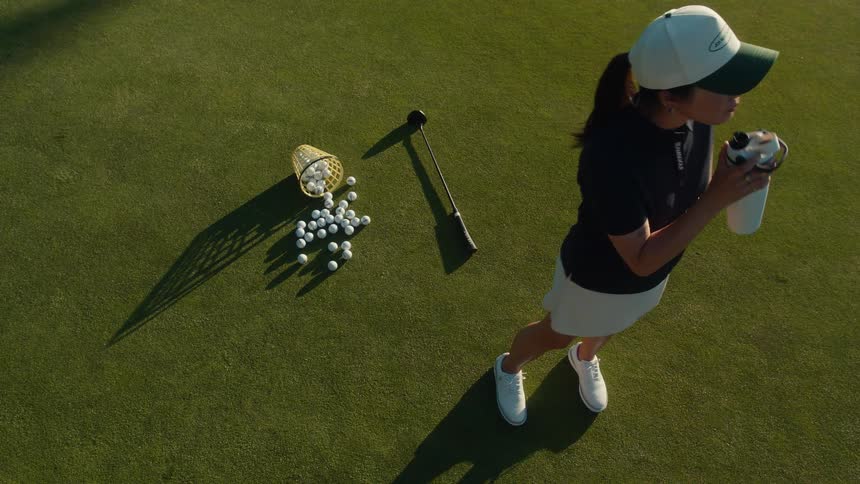 High angle slow motion shot of a woman golfer drinking water on the putting green on a sunny day
