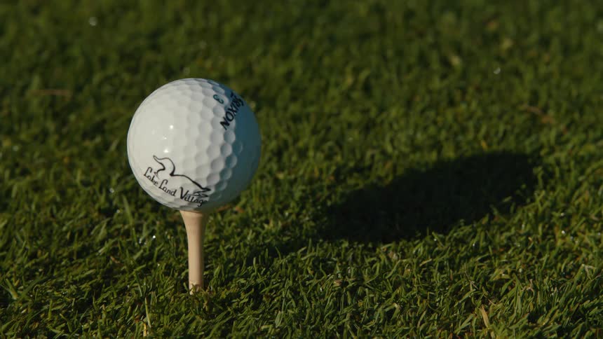 A golfer's hand carefully places a white golf ball on a wooden tee in the lush green grass