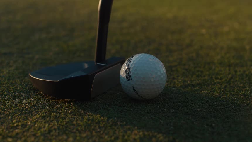Cinematic slow motion close-up of a golf putter striking a ball on the putting green at sunset