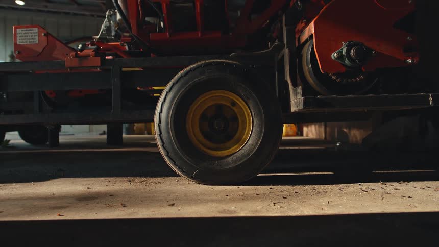 A static, low-angle shot shows a yellow-rimmed tire on farm machinery resting on a dusty concrete floor inside a barn