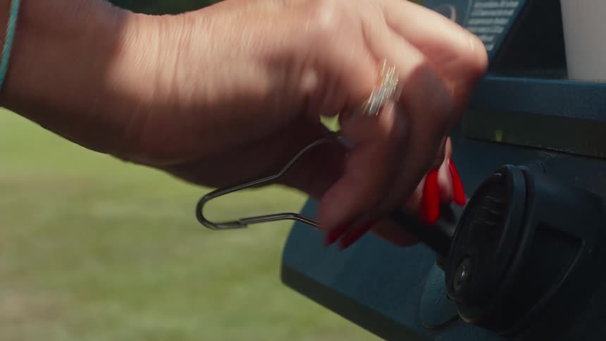 A woman's hand with red nails turns the key in the ignition of a golf cart on a sunny day