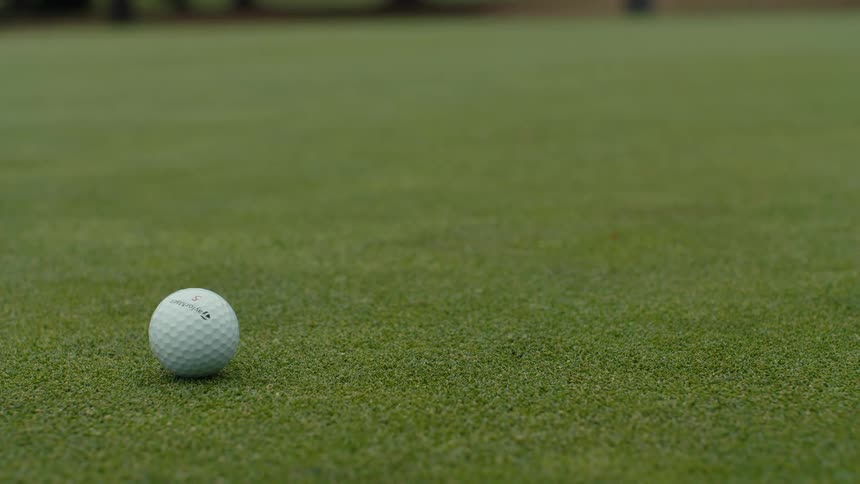 A white golf ball rolls slowly across a lush green putting surface and comes to a complete stop