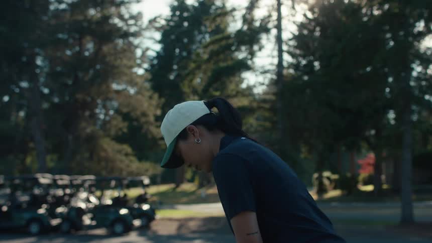 A young woman wearing a cap concentrates on her shot while playing golf on a sunny day