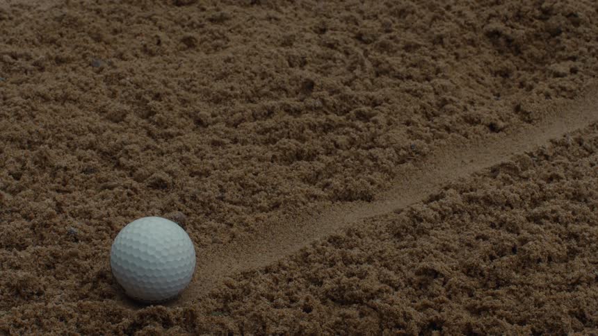 A stationary close-up shot of a white golf ball in a brown sand bunker next to a line drawn for practice