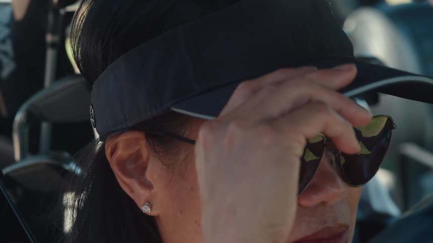 Close-up of a female golfer wearing a visor and sunglasses, adjusting them on a sunny day