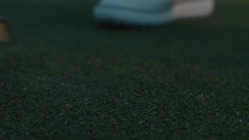 A close-up slow-motion shot of a golfer placing a golf ball with their shoe and lining up a putt on the green