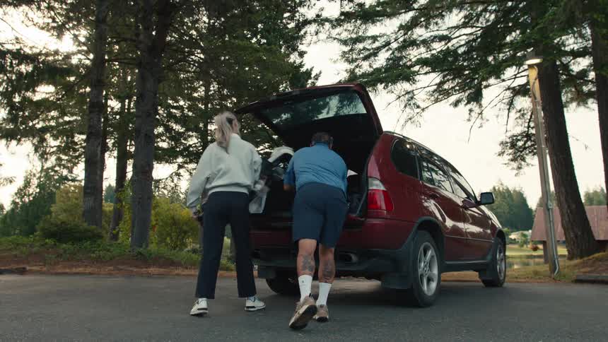 A man and woman unload their golf bags from the trunk of a red SUV in a parking lot, preparing for a round of golf