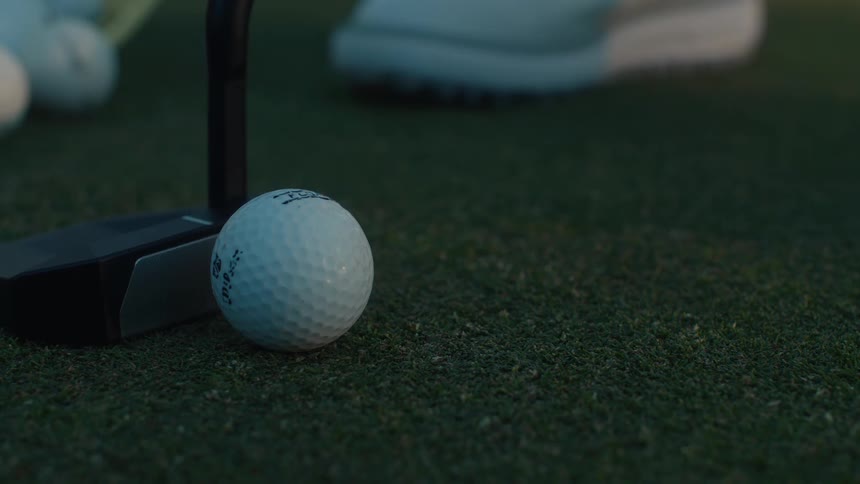 A golfer practices putting in slow motion, hitting multiple golf balls on the green