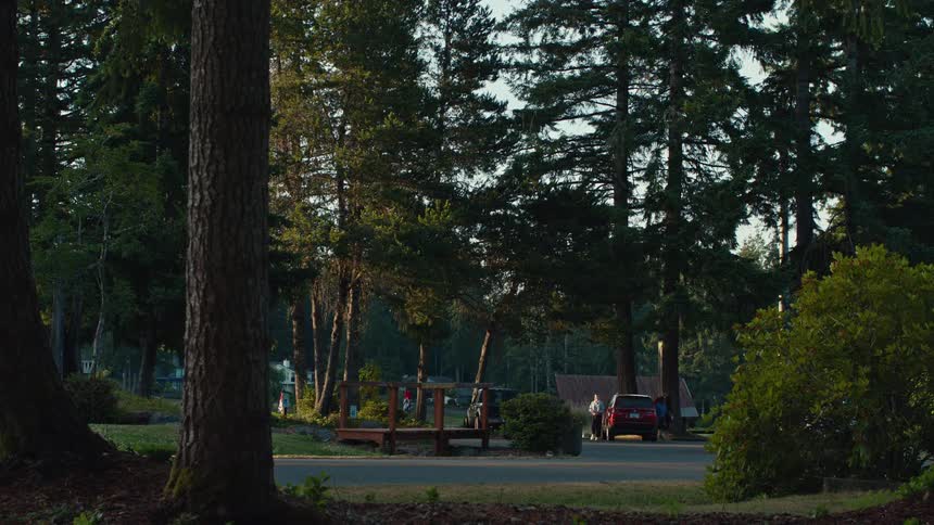 A red SUV drives down a peaceful, tree-lined road, parks, and people get out to unload their vehicle