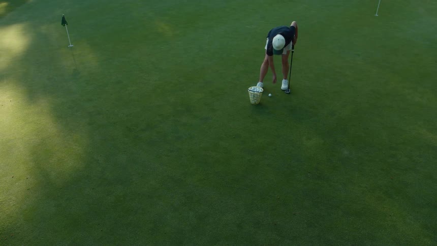 A woman golfer practices her putting on a perfectly manicured green, hitting balls from a bucket