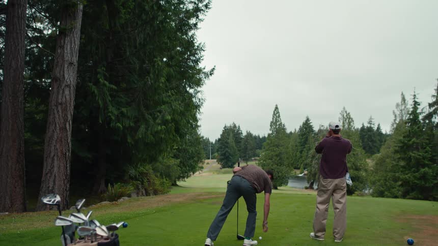 A golfer tees off with a driver on a lush course while his partner watches