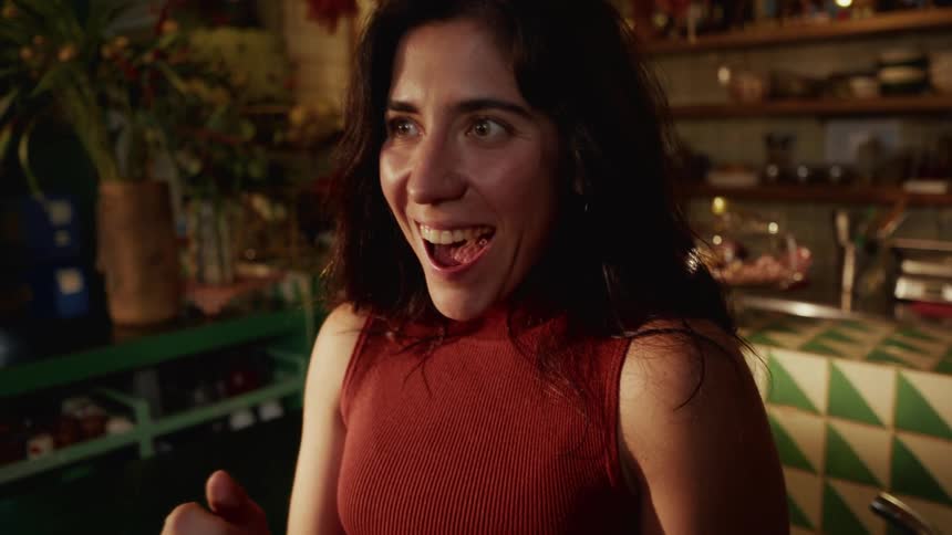 A young woman sitting in a cafe reacts with pure joy and excitement to something she sees on her smartphone