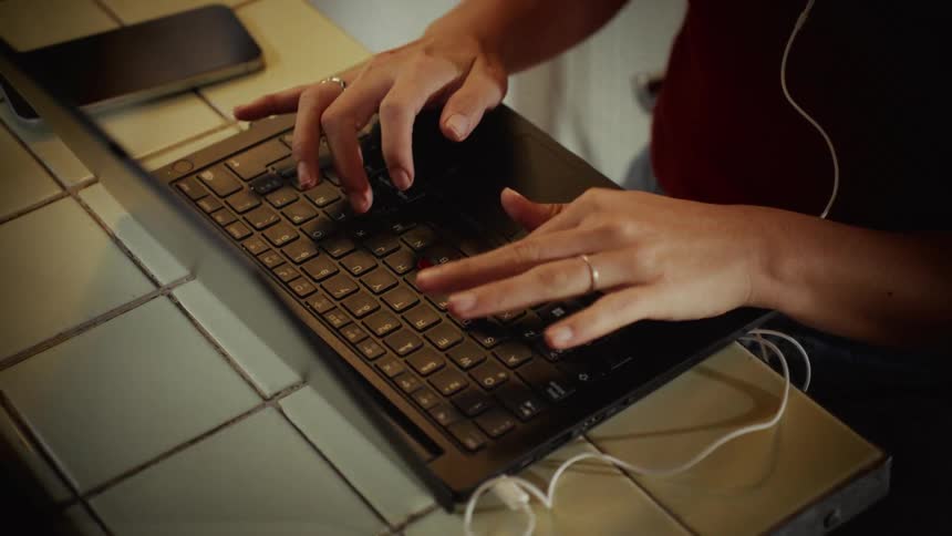 A close-up, high-angle shot of a person's hands typing on a laptop keyboard on a tiled counter