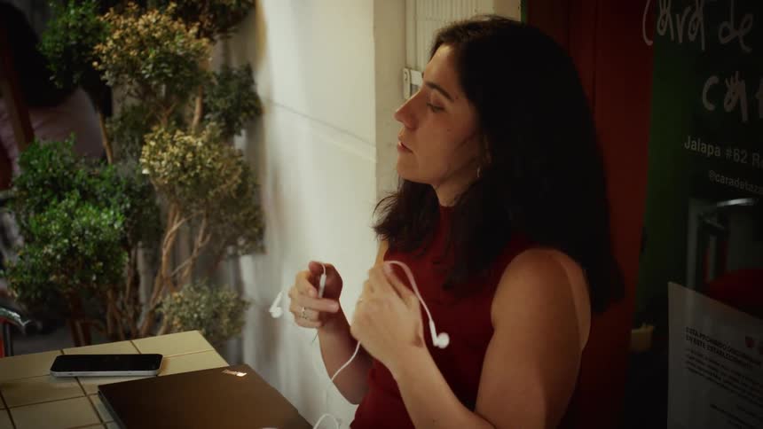 A woman in a red top slowly closes her laptop and takes off her earphones after working at an outdoor cafe