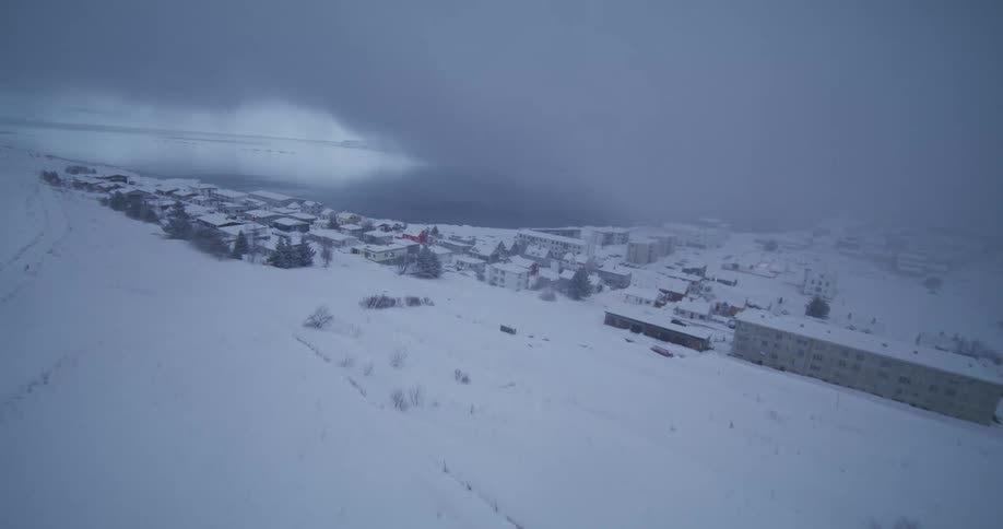 An aerial view reveals a snow-covered coastal town in Iceland during a foggy winter day