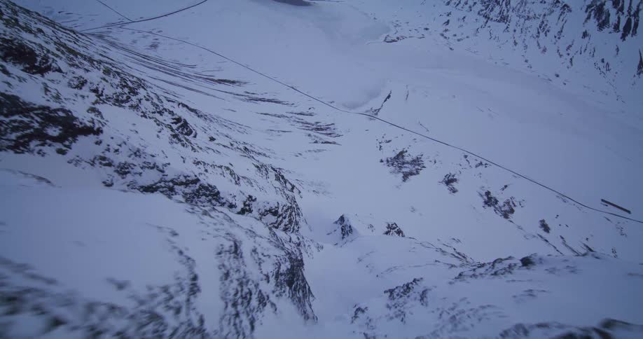 A sweeping aerial view pulls back over a snowy mountain ridge revealing a vast frozen valley and three skiers below