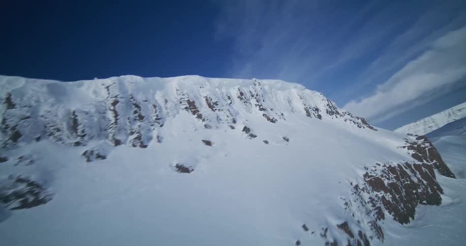 An immersive first-person aerial flight along a rugged, snow-covered mountain ridge under a vast blue sky