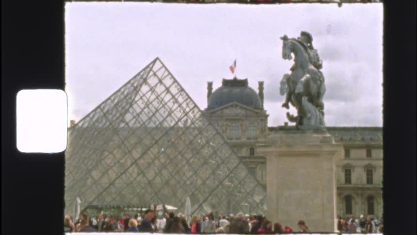 Vintage 8mm film captures a crowd of tourists gathered at the iconic Louvre Pyramid and museum in Paris, France