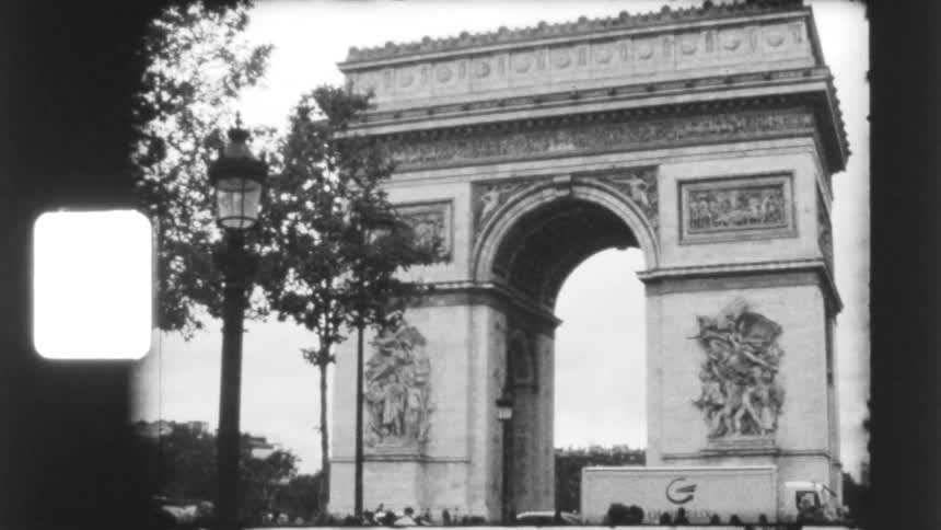 A vintage black and white archival film shot zooms out from the detailed sculptures to reveal the full Arc de Triomphe in Paris