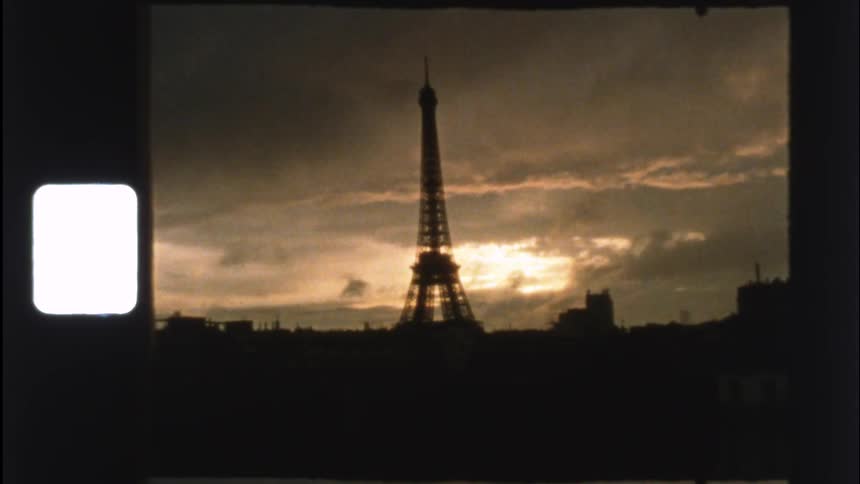 A vintage 8mm film captures the iconic Eiffel Tower silhouetted against a golden sunset sky as the camera zooms out