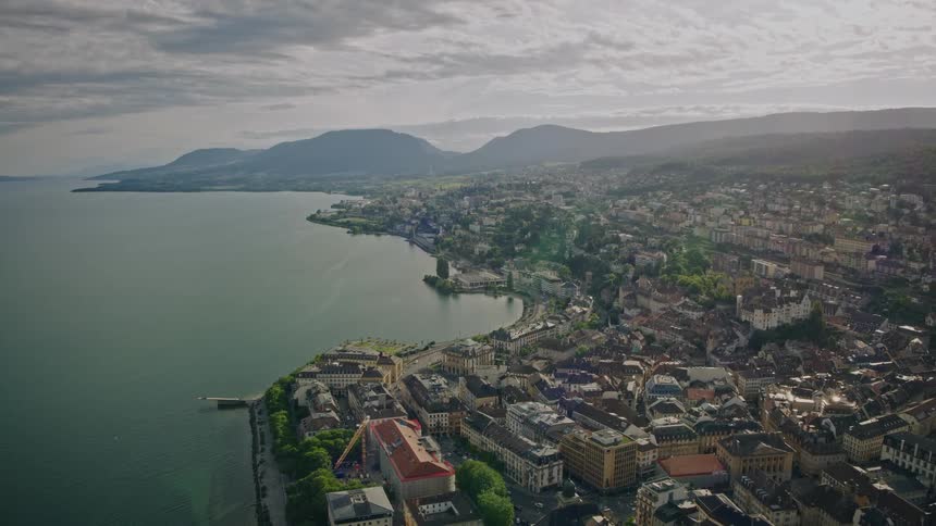 A static high-angle aerial view of the historic city of Neuchâtel, Switzerland, situated on the picturesque shore of a large lake with mountains in the distance