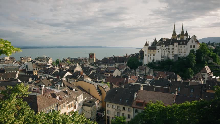 A scenic aerial view reveals the historic city of Neuchâtel, Switzerland, with its magnificent castle overlooking the lake and rooftops