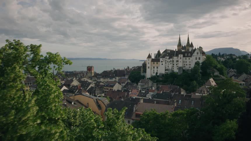 Slow aerial push-in shot revealing the historic city and castle of Neuchâtel overlooking the vast lake on a cloudy day
