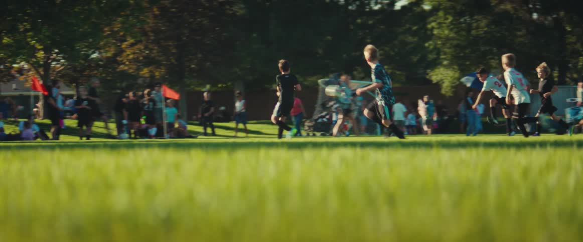 A side view of young boys playing a soccer match on a sunny day, culminating with a shot on goal that misses