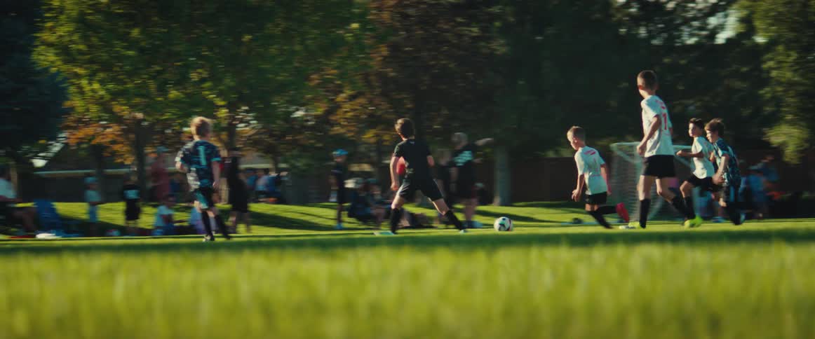 In an epic slow-motion shot, a young boy dribbles the soccer ball down the field, past defenders, and takes a shot on goal