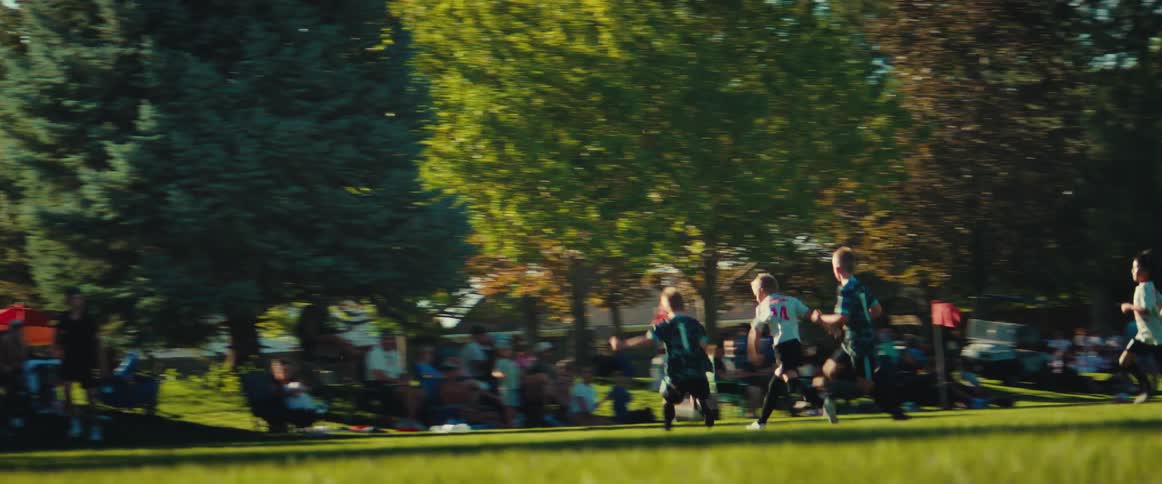 A cinematic pan follows young boys running with the ball during a competitive soccer game as spectators watch from the sidelines