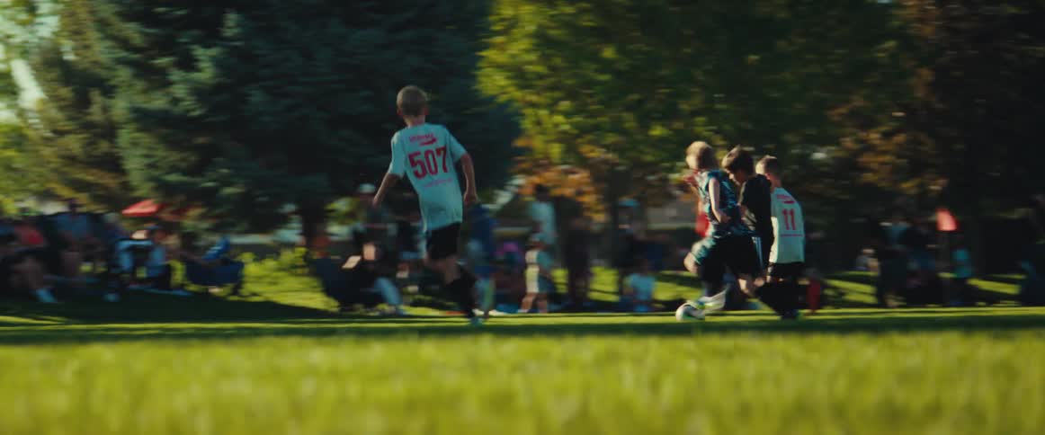 Energetic low-angle tracking shot of young boys competing in a soccer match on a sunny grass field