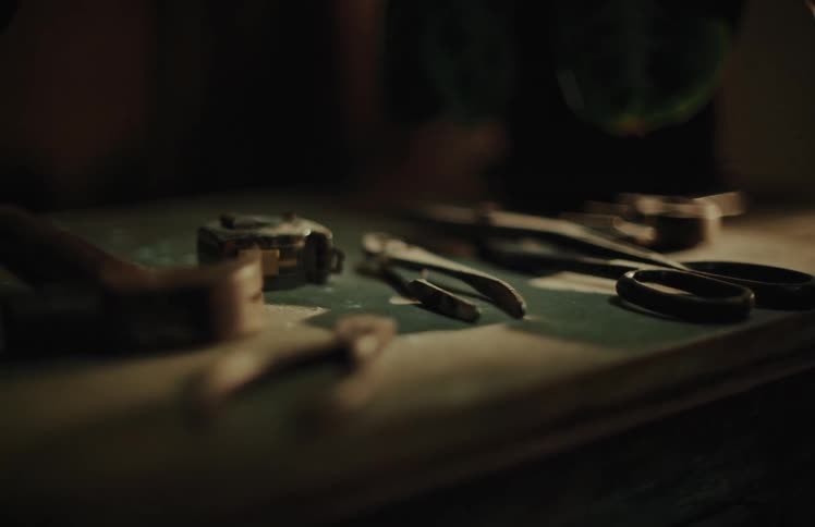 A moody, slow-motion rack focus shot reveals various hand tools on a workbench as water drips from a plant above