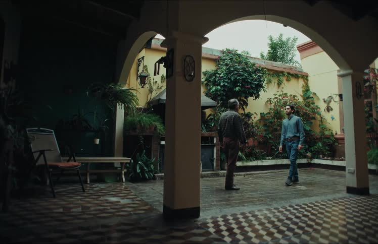 An older father and his adult son reunite and share an emotional hug in the open-air courtyard of a traditional home