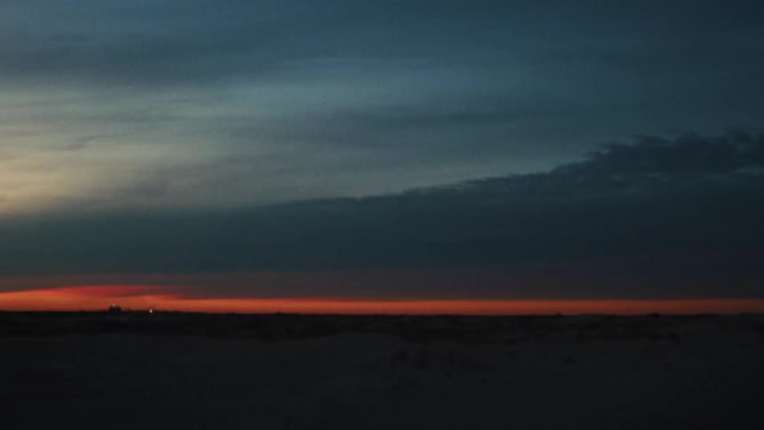 A thin line of vibrant orange afterglow illuminates the horizon under a vast, dark twilight sky