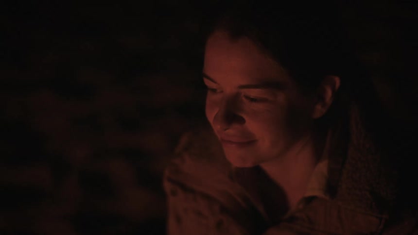 Close-up of a contemplative woman's face glowing in the warm light of a campfire at night