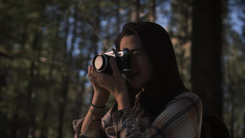 A young female photographer takes a picture with a vintage film camera in a sunlit forest in slow motion