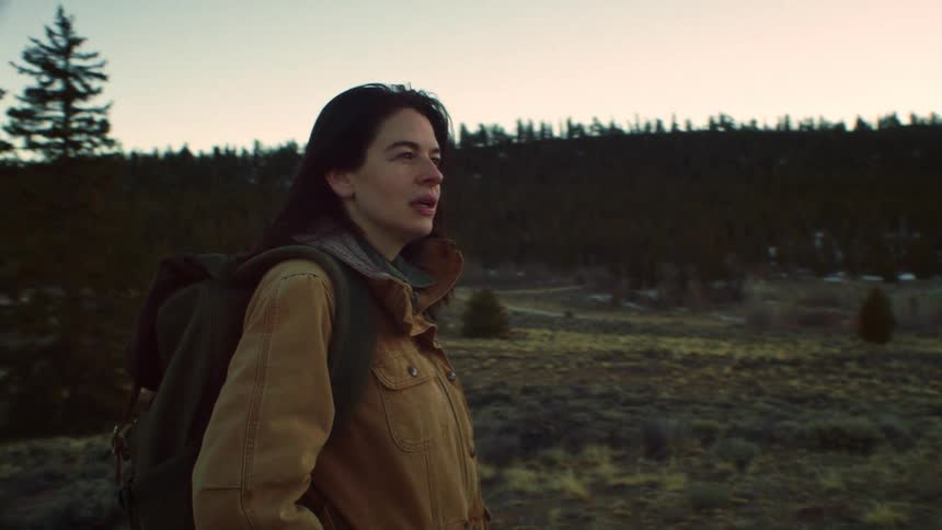 A lone female hiker with a backpack takes a contemplative walk through a rugged wilderness meadow at sunrise