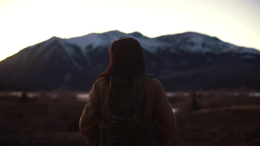 A lone traveler with a backpack pauses to admire the view of a majestic snow-capped mountain at dusk