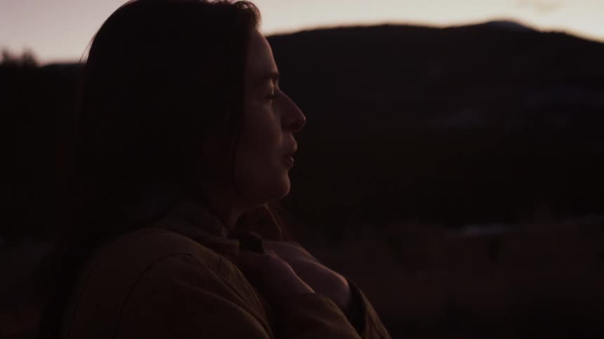 A serene woman in silhouette smiles while enjoying a peaceful moment in the mountains at dusk