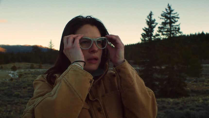 A woman stops in a beautiful wilderness meadow at sunset, putting on her glasses in slow motion to admire the view