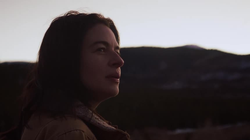 A thoughtful woman smiles and reflects peacefully while watching the twilight fade over the mountains