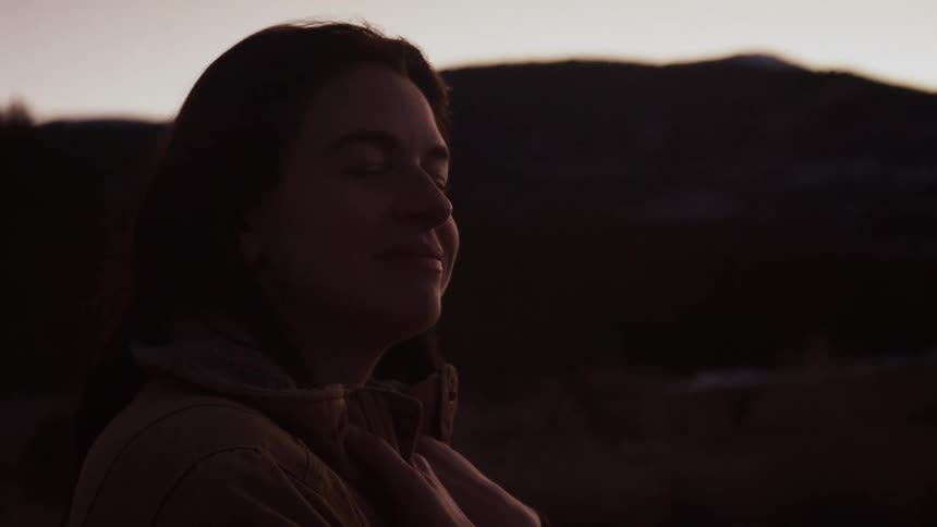 A serene woman takes a peaceful moment to breathe in the mountain air as the sun sets