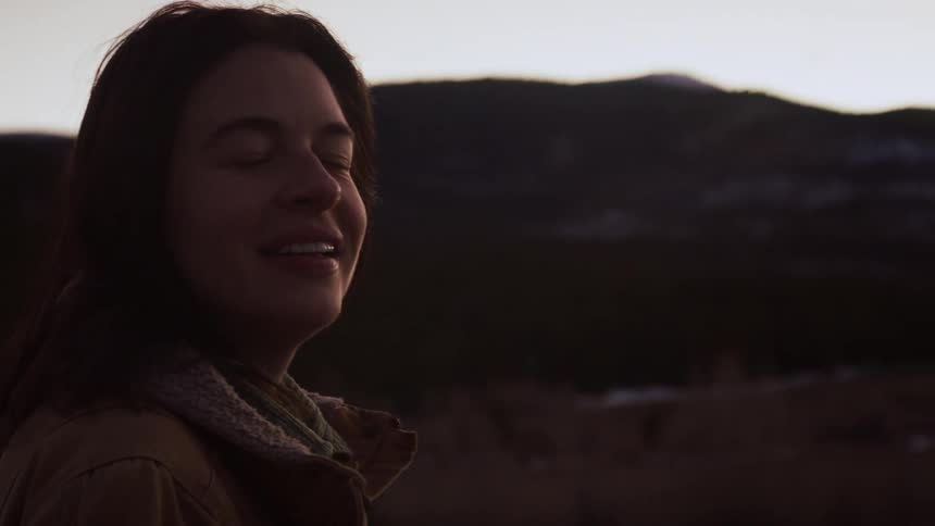 A happy woman smiles peacefully as she breathes in the fresh mountain air at dusk in slow motion