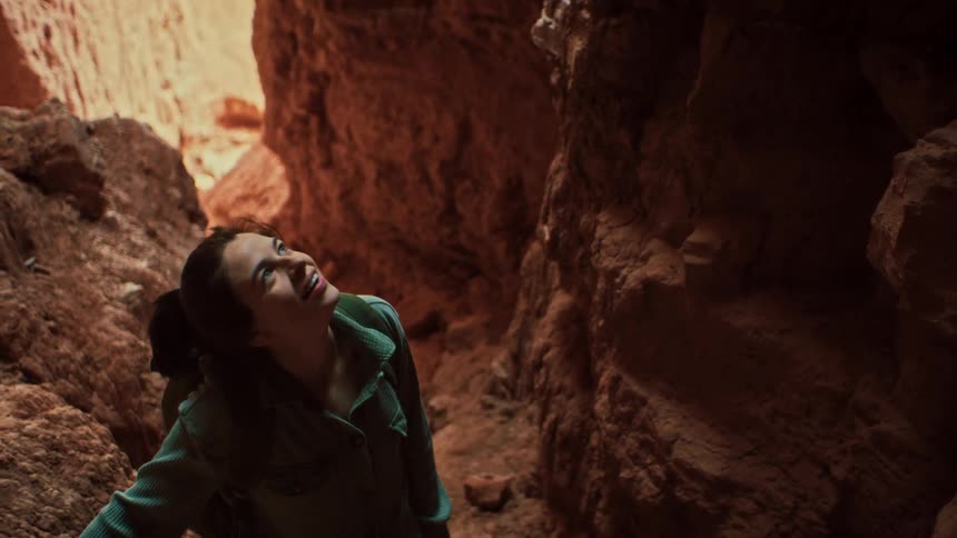 A happy young female hiker looks up in awe and wonder while exploring a narrow red rock slot canyon