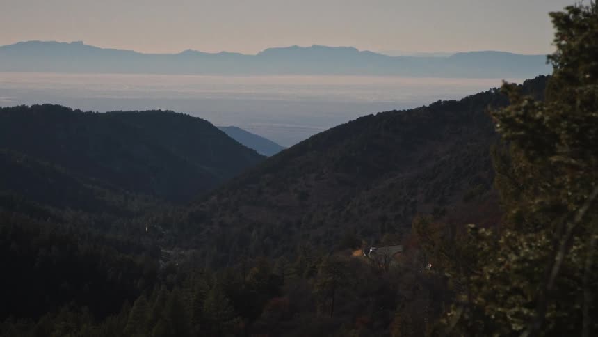 Cars with headlights on navigate a winding road through a vast mountain valley with a hazy, distant landscape