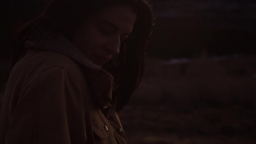 A serene woman bundled in a warm jacket closes her eyes and smiles, finding a moment of peace in the mountains at twilight