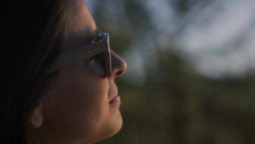 A close-up profile of a serene woman in smart glasses looking up thoughtfully, her face illuminated by the warm glow of a beautiful sunset