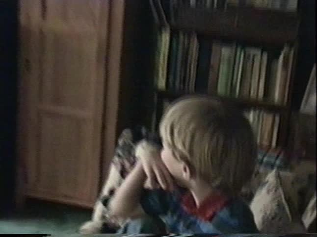 Vintage VHS footage captures a young boy sitting on a couch, engrossed in watching an old television in a retro living room