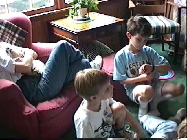A candid home video from the 90s shows two young boys sitting on the floor in a living room as one plays with a toy